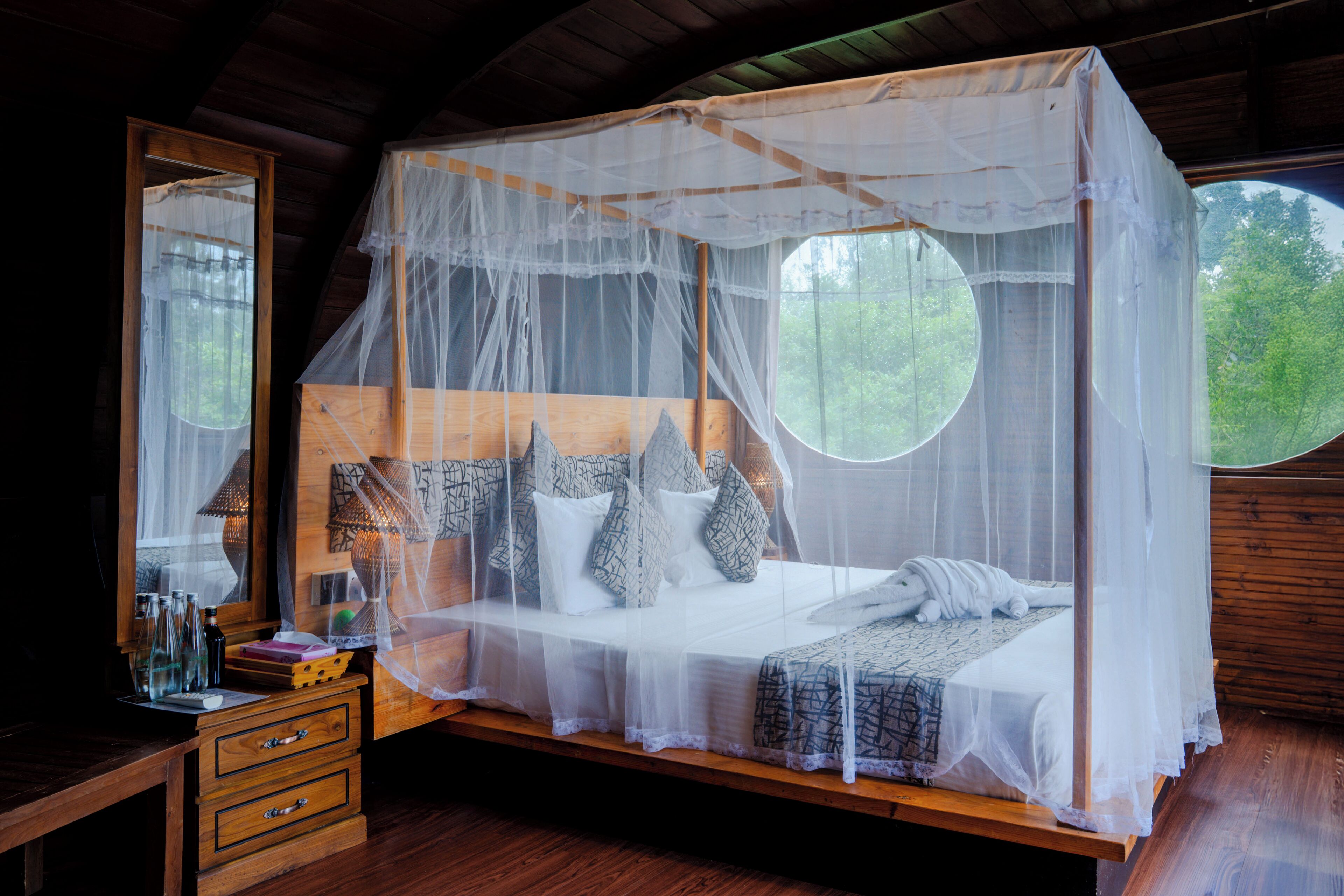 A wooden four-poster bed with a mosquito net, a bedside table with bottles, and a mirror.
