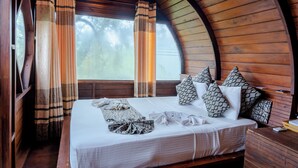 Une pièce chaleureuse avec un plafond en bois aux lignes courbes, un grand lit agrémenté d’oreillers à motifs et des rideaux.
