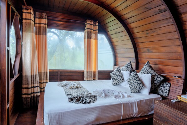 A cozy room with a curved wooden ceiling, a large bed with patterned pillows, and curtains. - Leopard Nest in Yala (Tissamaharama)