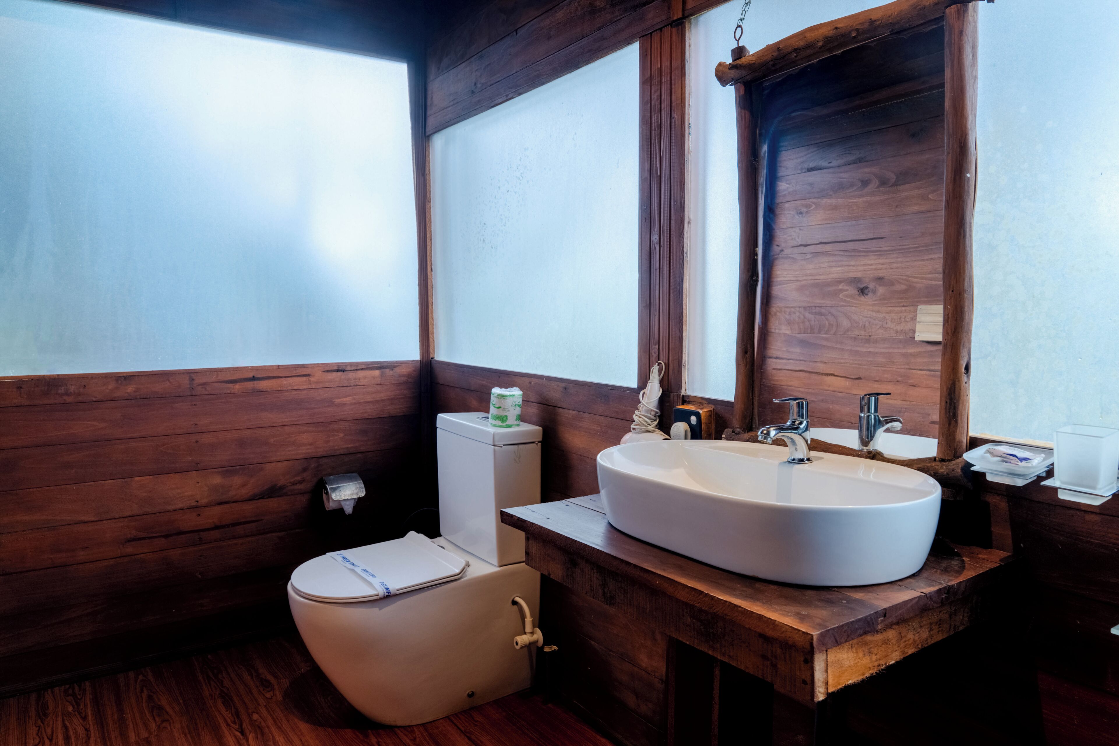 A wooden bathroom with a white sink, two faucets, and a mirror.