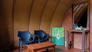A tented room with two blue chairs, a wooden table, a painting, and a small wooden table with bottles. - Leopard Nest in Yala (Tissamaharama)