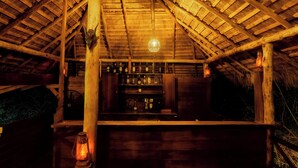 Un intérieur avec un plafond en bois, un coin bar avec des bouteilles et un luminaire suspendu.