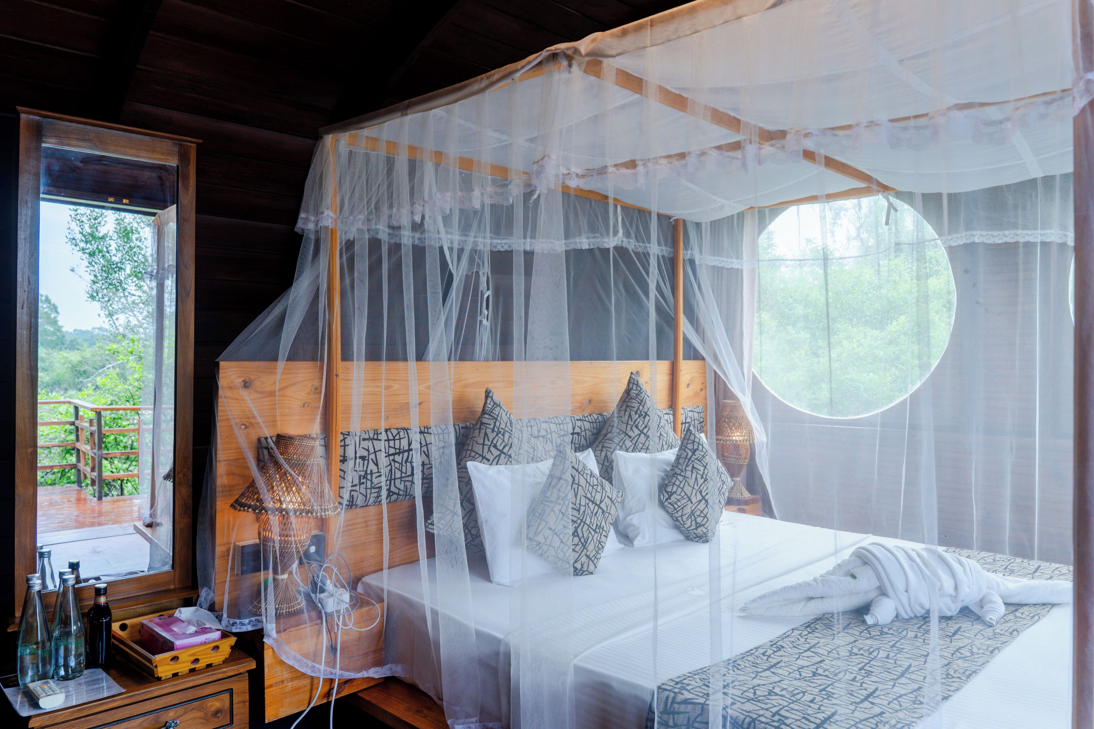 Un dormitorio con cama a dosel, cabecera de madera y mesita de noche con botellas y una lámpara.