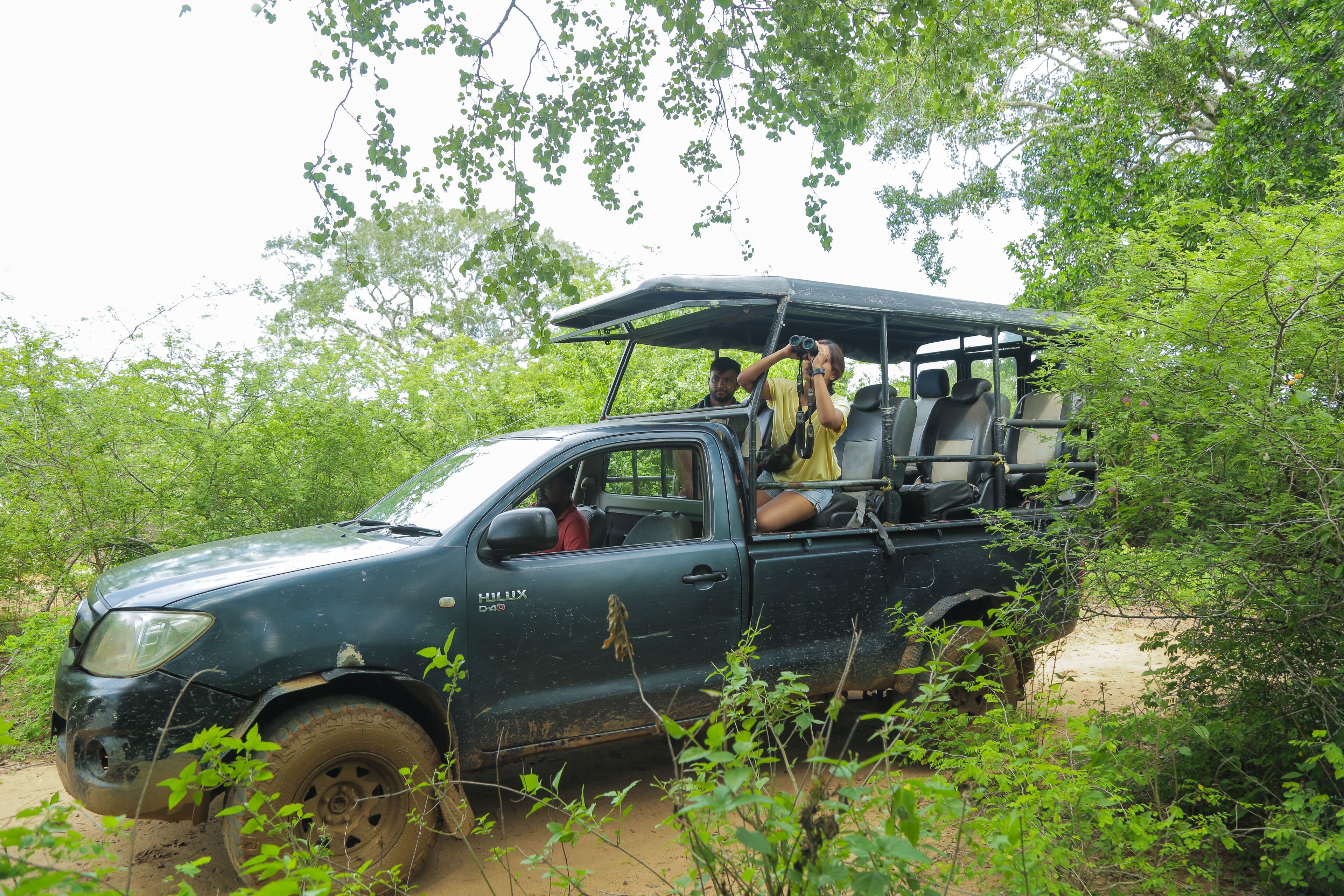 A dark green pickup truck with a roof rack and passengers, parked in a forested area.