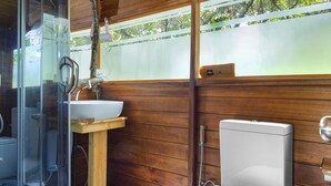 A compact bathroom with a glass-enclosed shower, a sink, and a toilet. - Leopard Nest in Yala (Tissamaharama)