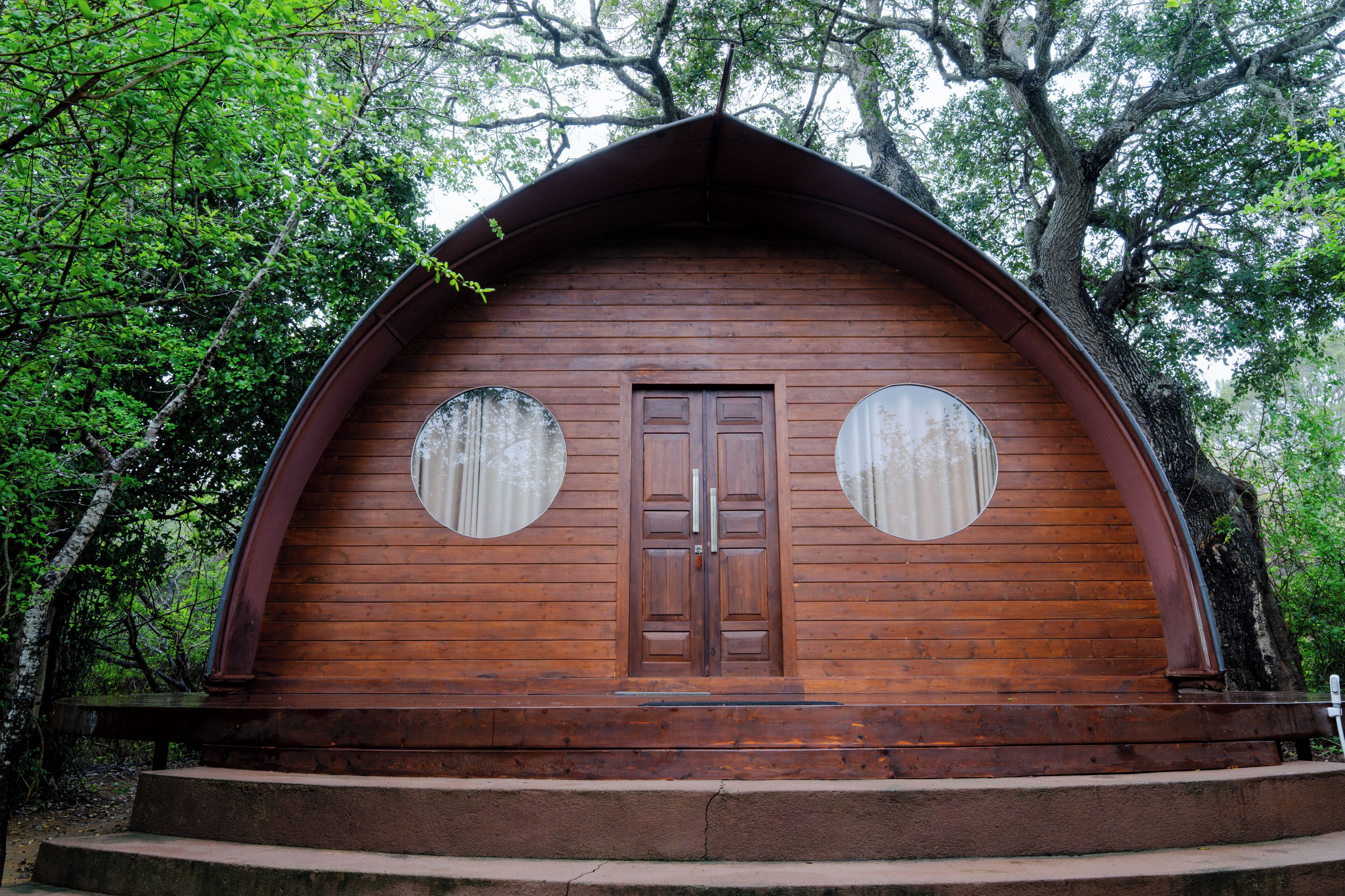 Una cabaña de madera con techo a dos aguas, dos ventanas circulares y una puerta de madera.
