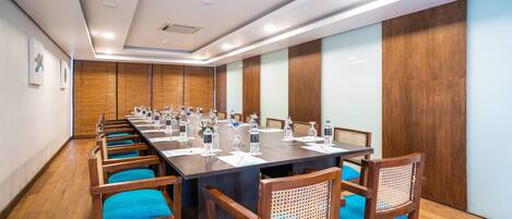 A conference room with a long table, wooden chairs with blue cushions, and a wooden panel wall.
