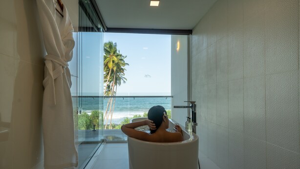 A bathtub with a view of the ocean and palm trees.
