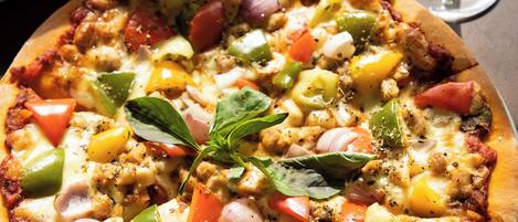 Una pizza con distintos ingredientes sobre un plato blanco, acompañada de una copa de vino blanco y una servilleta doblada.