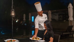 A chef serving a dish to a guest at an outdoor dining table with a view of the night sky.