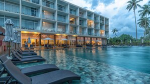 A hotel with a swimming pool, lounge chairs, and umbrellas.