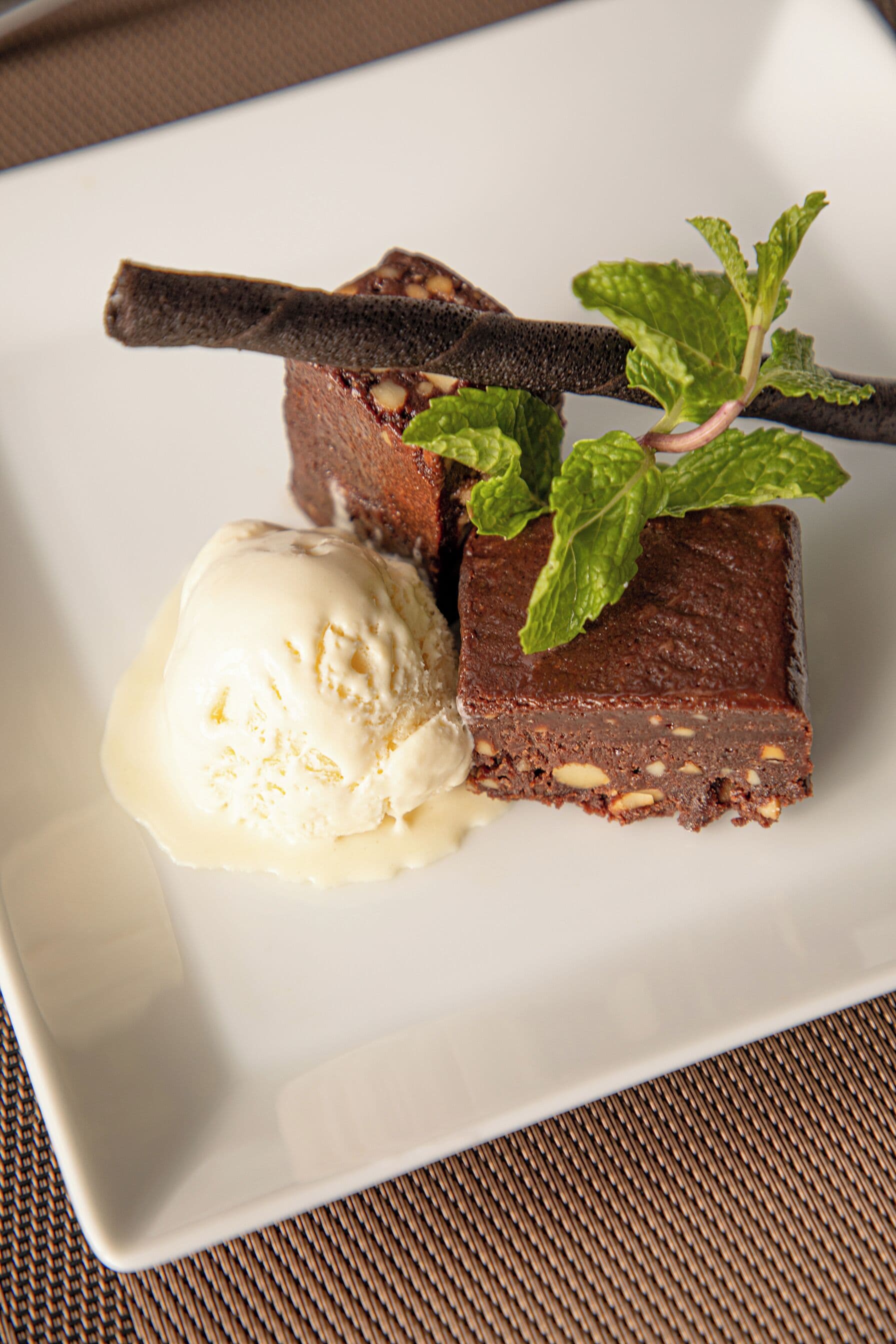 Prato de sobremesa com um brownie, uma bola de sorvete de baunilha e um toque de hortelã.