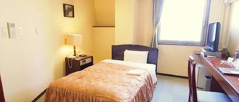 Habitación de hotel con cama, escritorio, silla, lámpara, ventana con cortinas e imagen en la pared.