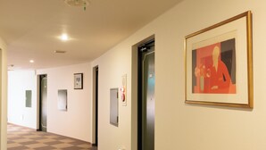 Un pasillo con suelo de cuadros, obras de arte enmarcadas en la pared y un ascensor.