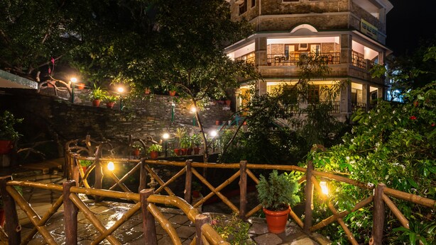 Un immeuble à plusieurs étages, doté d’une façade en pierre, d’un balcon à l’étage supérieur et d’une clôture en bois, avec des plantes en pot disposées au premier plan.