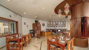Un grand espace à manger avec des tables et des chaises en bois, une cuisine à l’arrière-plan et des lanternes décoratives suspendues au plafond.