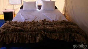A single bed with a brown bedspread, two pillows, and a nightstand with a lamp. - Nomad Camp (Leh)