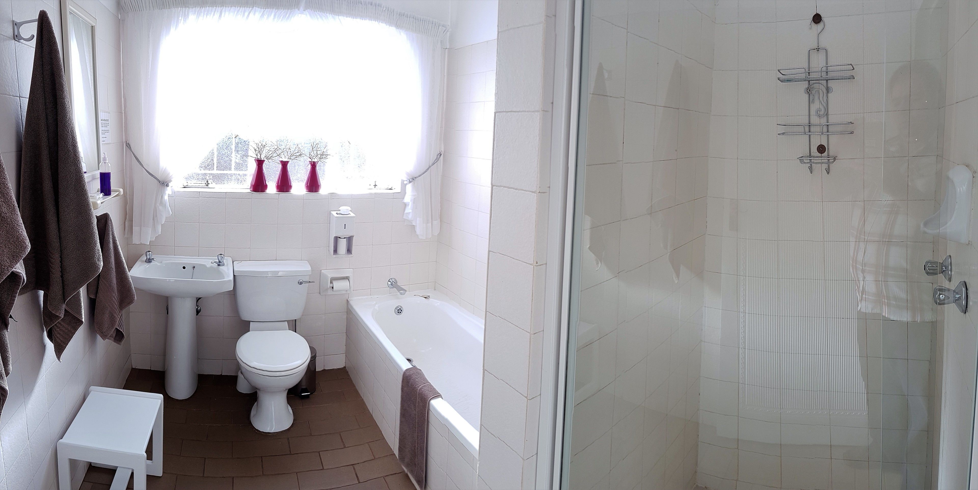 A bathroom with a toilet, sink, and bathtub. There is a window with curtains and three vases on the windowsill.