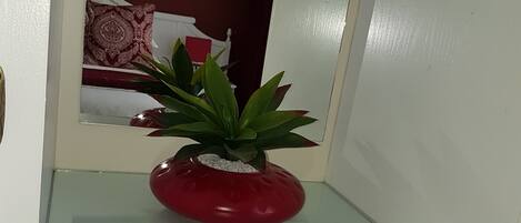 Un petit meuble blanc, doté d’un dessus en verre et contenant un seul pot rouge dans lequel se trouve une plante verte.