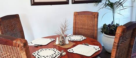 A dining area with a round wooden table, wicker chairs, and two framed rooster paintings on the wall.