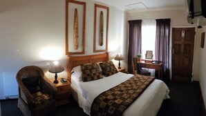 A hotel room with a large bed, two bedside tables with lamps, a wooden desk with a mirror, and a chair. - Eskulaap Hotel and Conference (Polokwane)