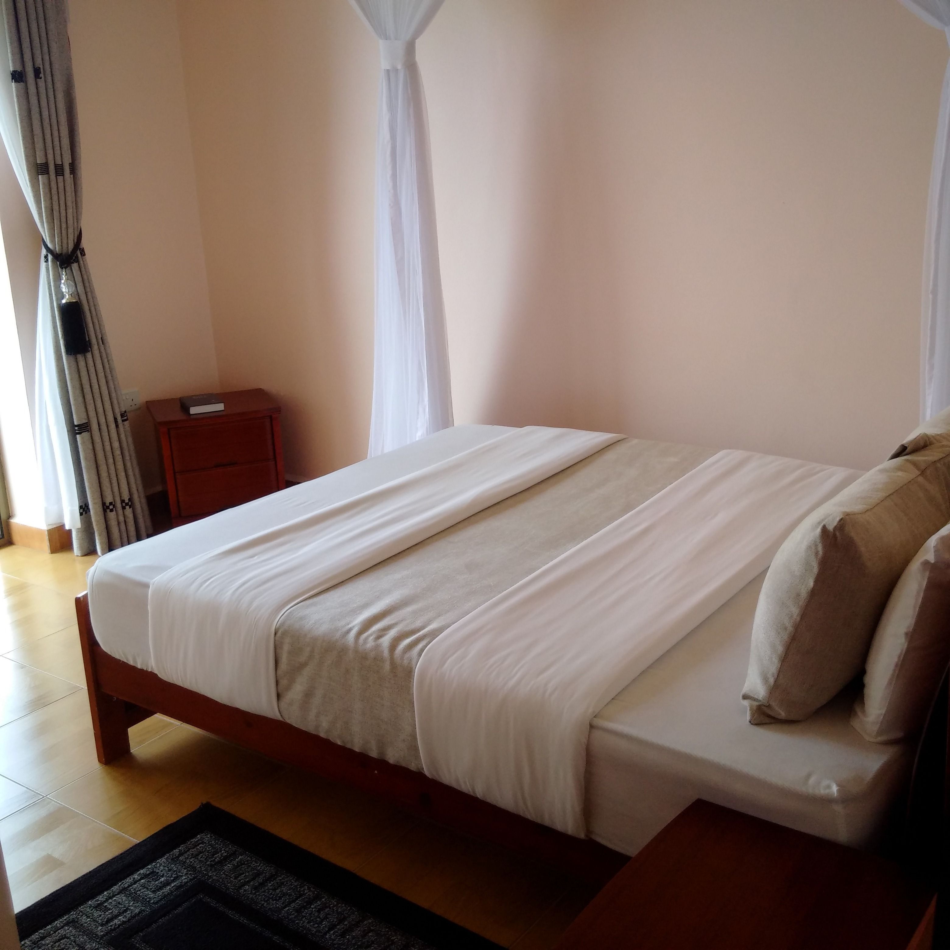 Een net opgemaakt bed met witte lakens, een houten nachtkastje en een klein bijzettafeltje.