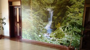 Un passadís amb un mural gran d'una cascada, un paviment de rajoles i una planta en test.