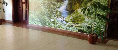 A hallway with a large mural of a waterfall, a tiled floor, and a potted plant.