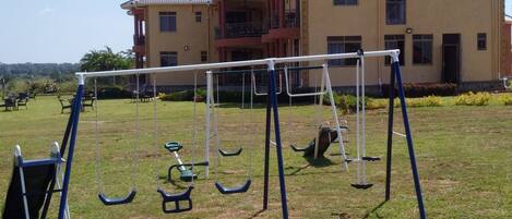 A playground with swings and a slide in front of a two-story building.