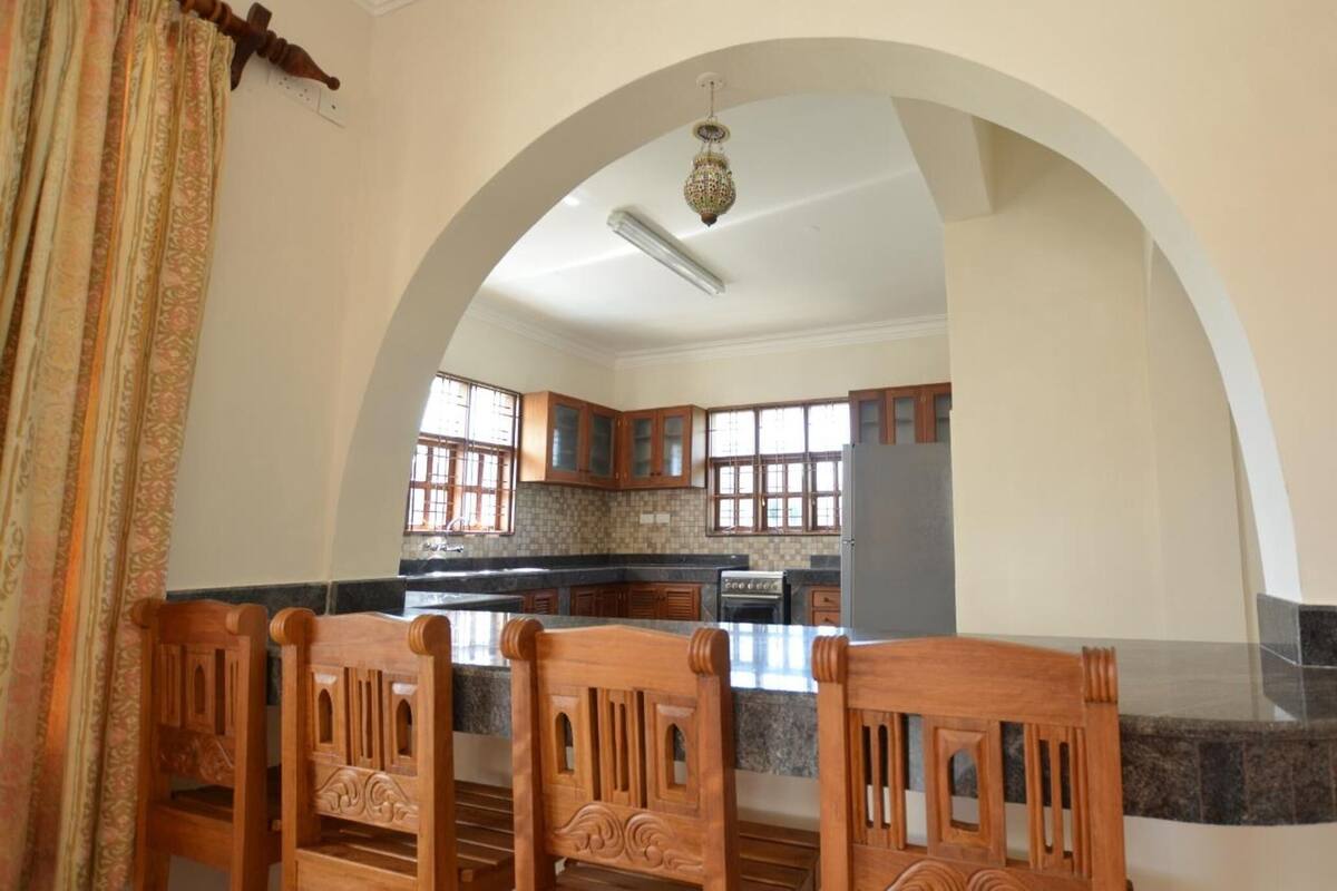 A spacious kitchen with an arched doorway, wooden chairs, and a granite countertop.