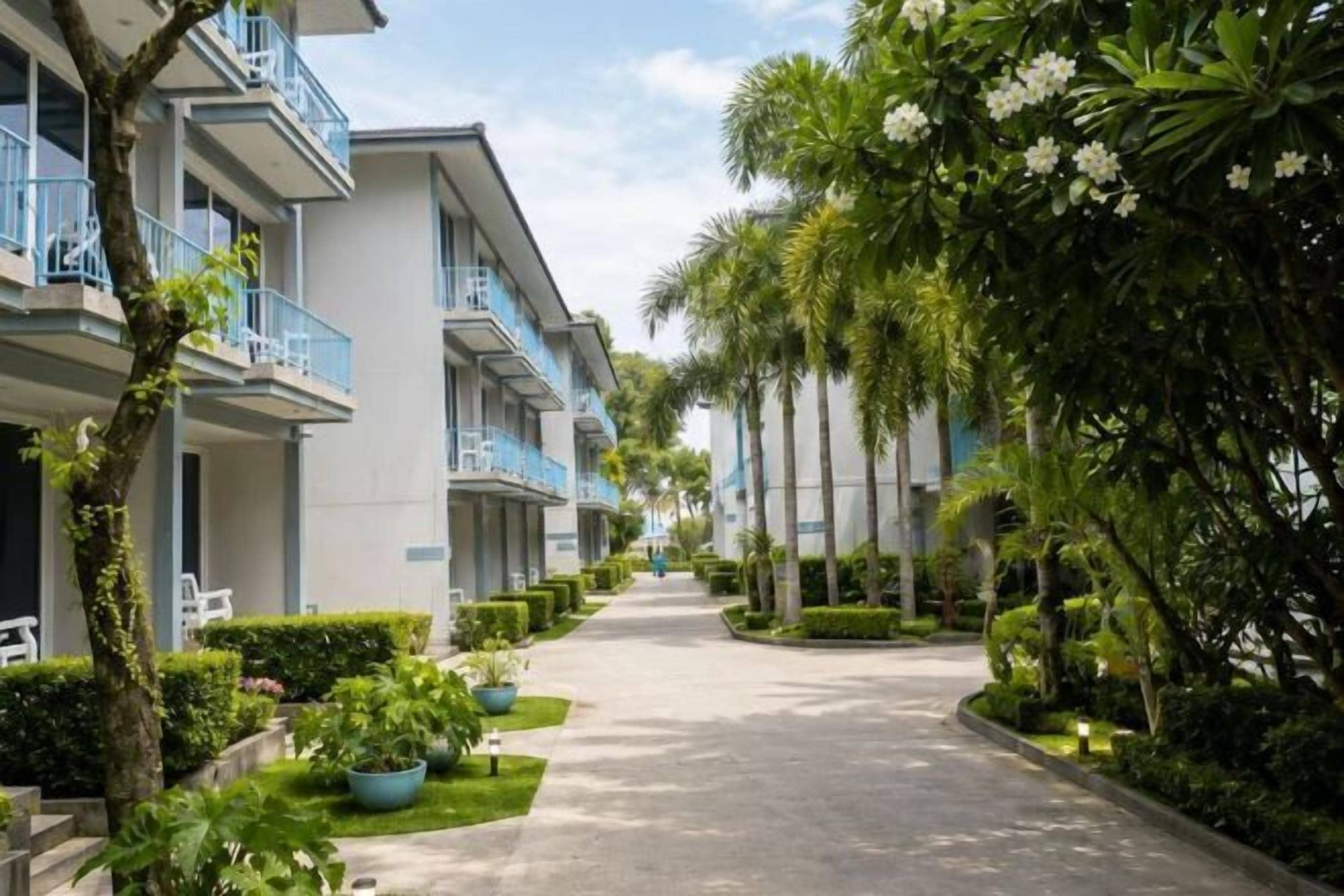 A row of hotel buildings with balconies, a paved walkway, and lush greenery.