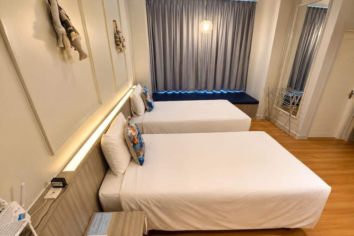 A hotel room with two beds, a desk with a lamp, a small table with a phone, and a window with curtains.