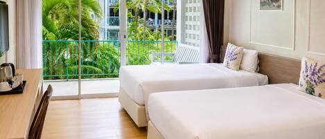 A hotel room with two beds, a desk with a coffee maker, and a view of a balcony with greenery.