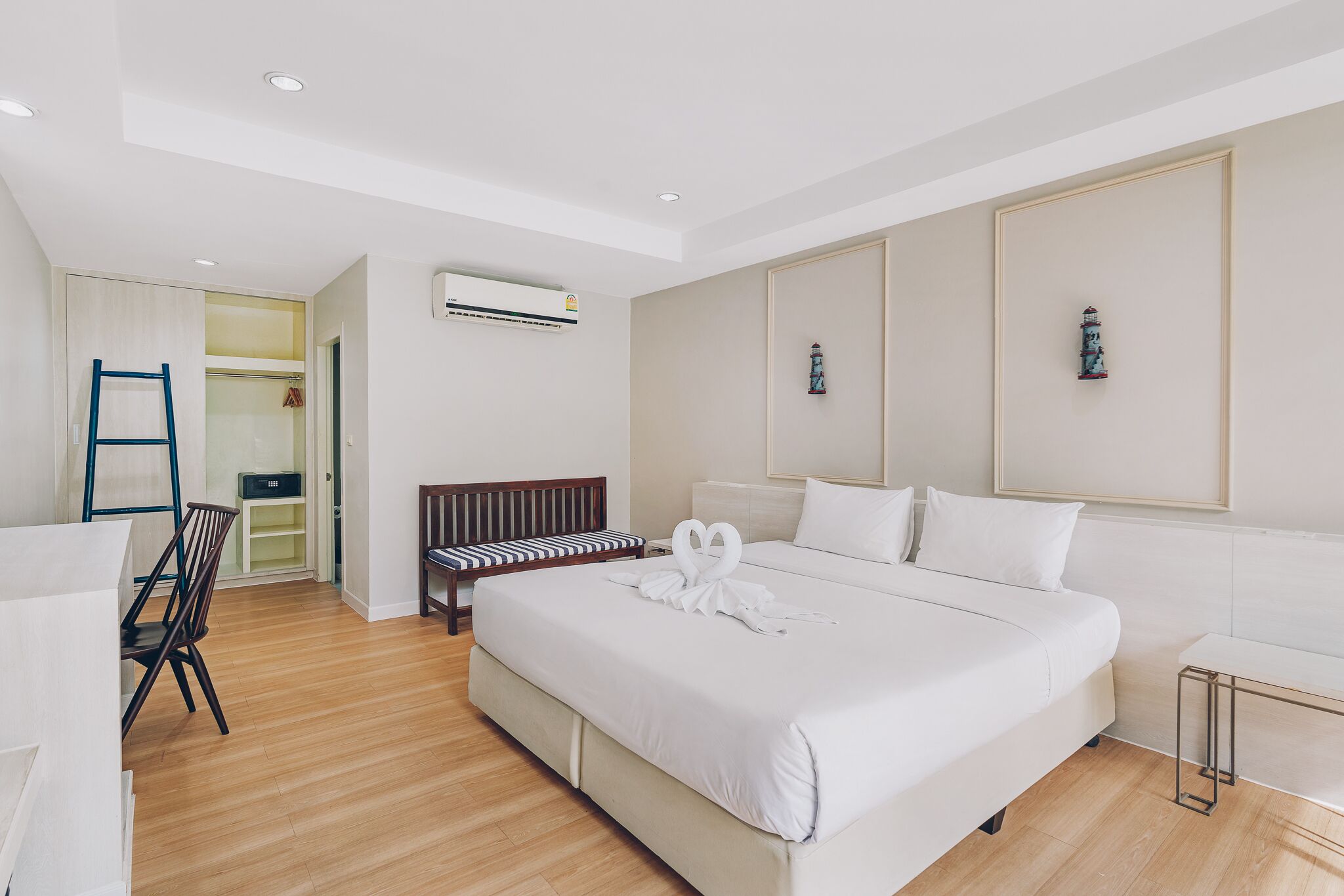A modern hotel room with a large bed, a desk, a chair, and a bench.