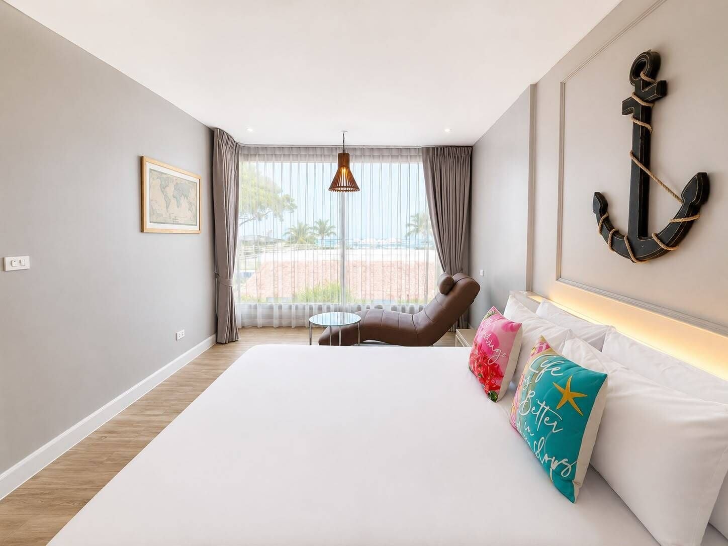 A hotel room with a bed, a chair, a small table, a hanging light, a framed picture, and a large anchor decoration.