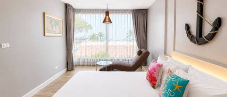 A hotel room with a bed, a chair, a small table, a hanging light, a framed picture, and a large anchor decoration.