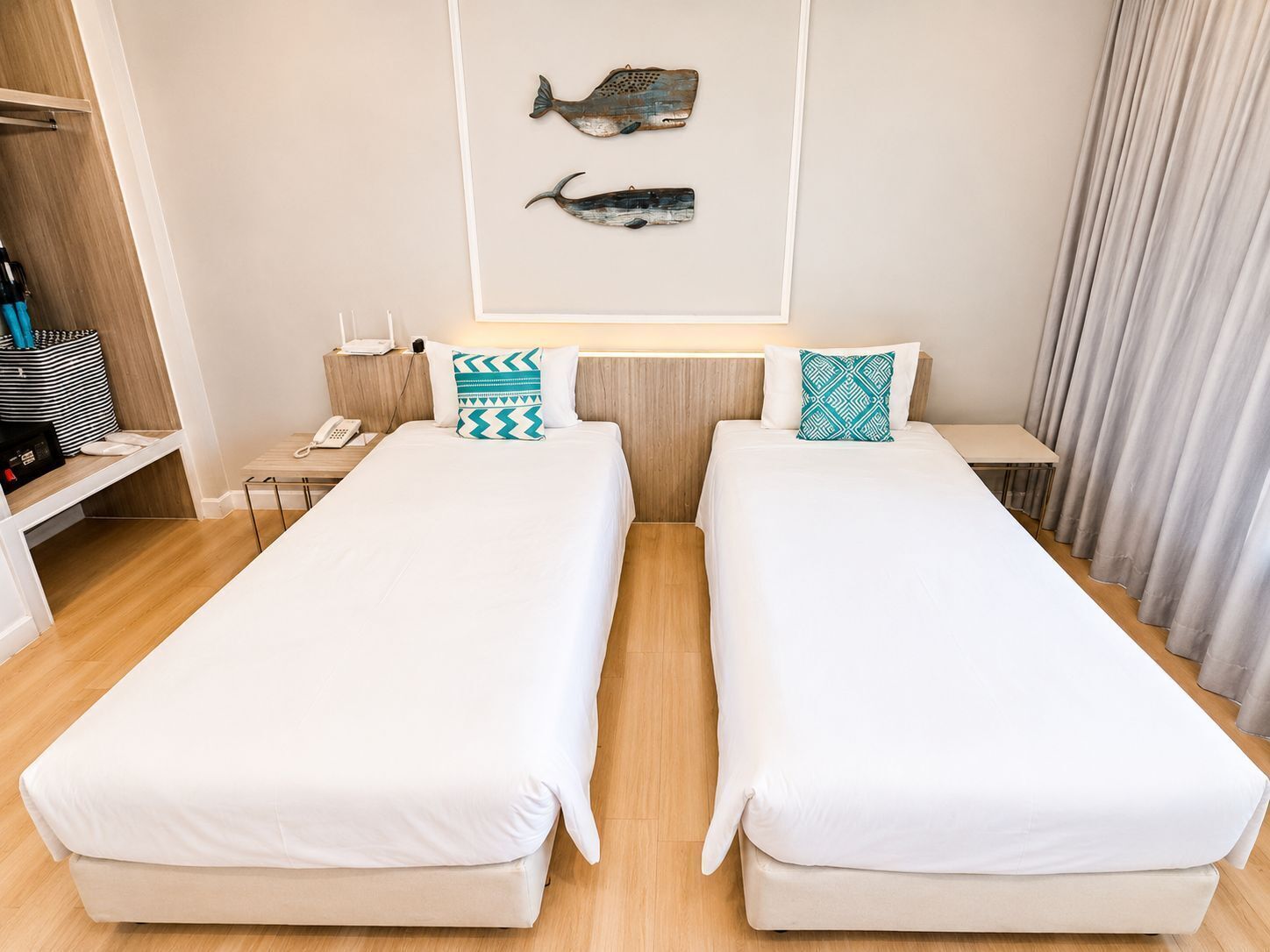 Une chambre d’hôtel avec deux lits simples, un bureau, une chaise, un téléphone, un porte-manteau et un décor mural représentant des poissons.