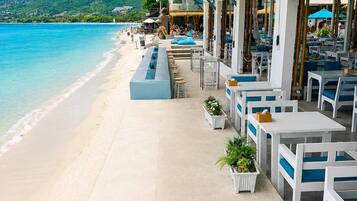 Un restaurante frente a la playa con terraza, piscina y vistas al océano y las colinas.