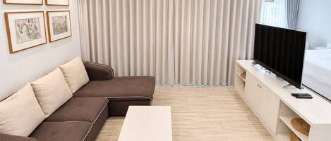 Una sala de estar moderna con un sofá modular, una mesa de centro blanca, un televisor de pantalla plana sobre un mueble blanco y obras de arte enmarcadas en la pared.