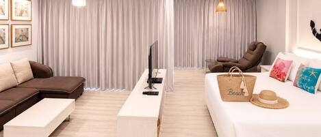 A modern hotel room with a sofa, a bed, a desk, a TV, and a chair.