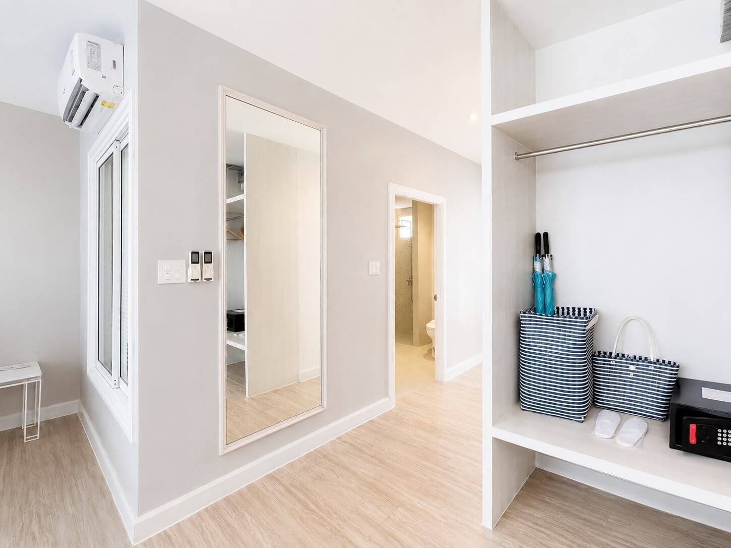 A modern, well-lit room with a large mirror, a white wardrobe, and a shelf with toiletries.