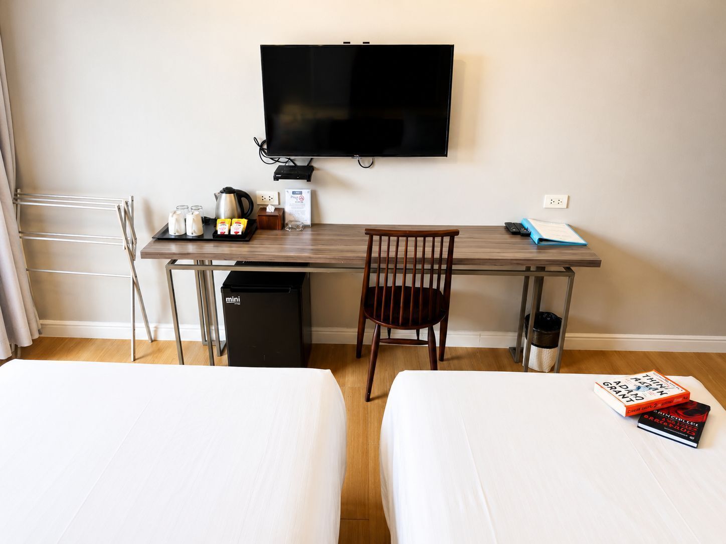 A hotel room with a bed, a desk with a chair, a TV, a mini fridge, and a trash bin.