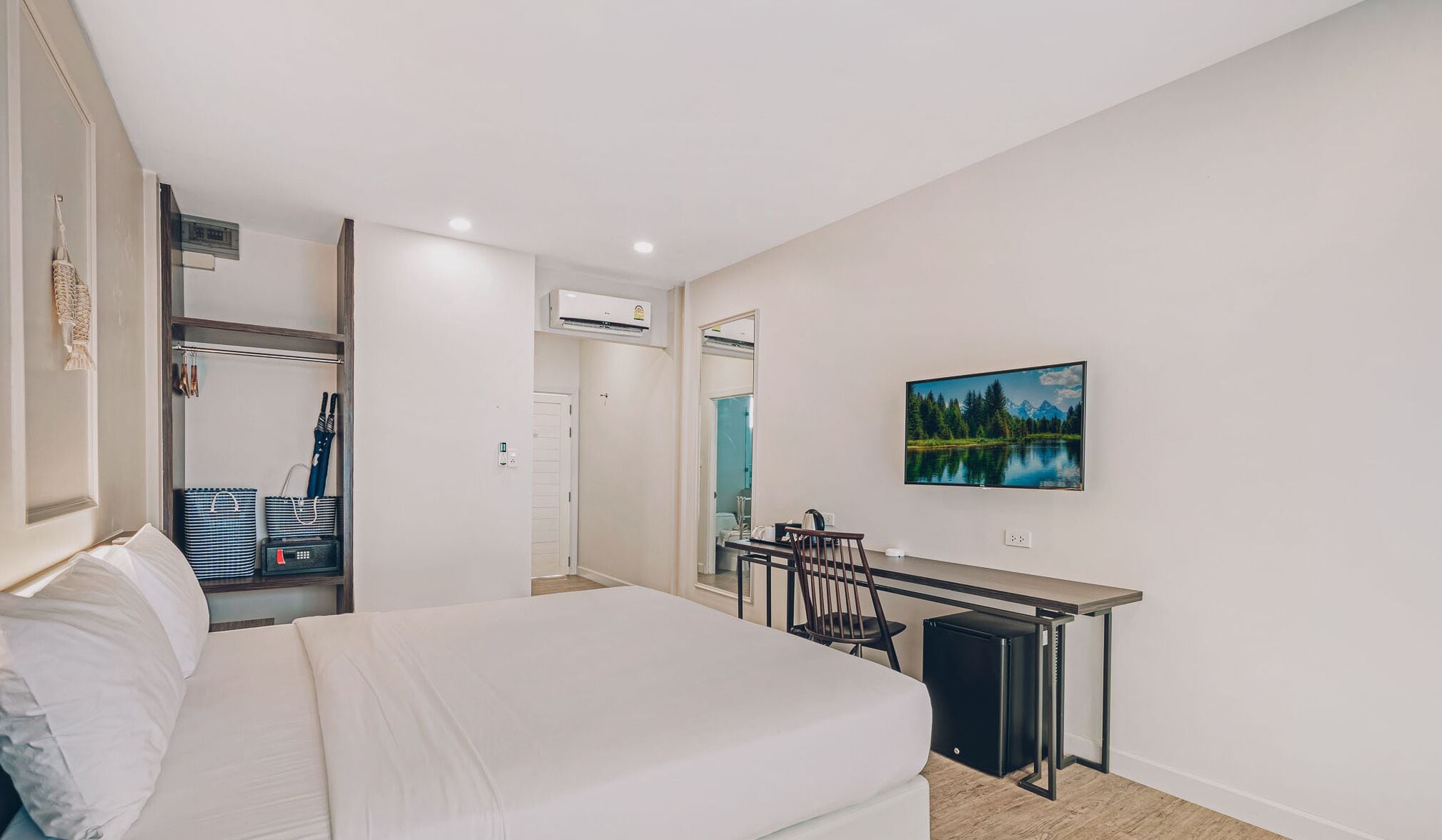 A hotel room with a bed, a desk with a chair, a TV mounted on the wall, and a painting of a lake.