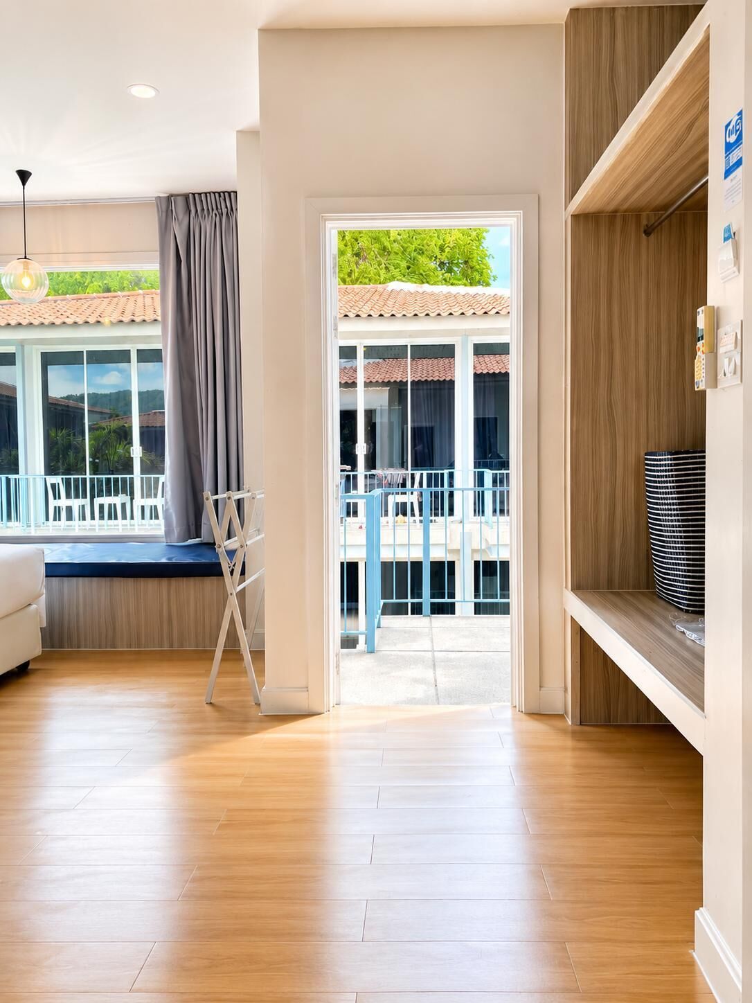 Une pièce moderne avec un plancher en bois, un canapé blanc, un banc bleu et une vue sur un balcon doté d’un toit en tuiles.