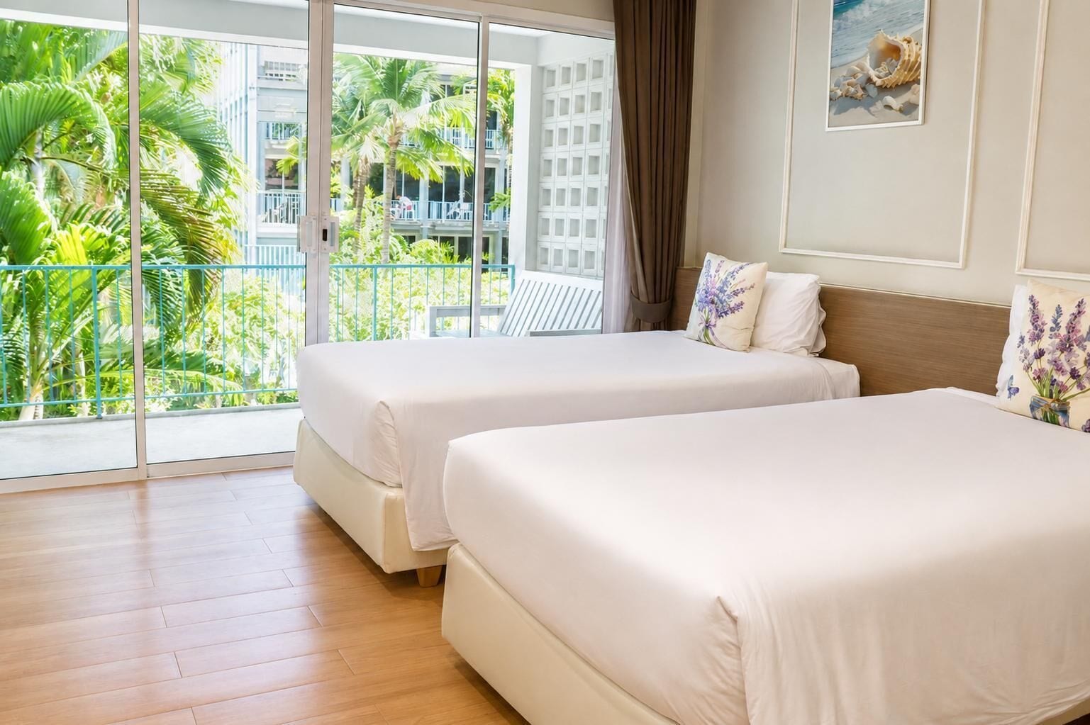 A hotel room with two beds, a balcony with a view of palm trees and a building, and a framed picture on the wall.