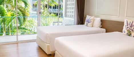 A hotel room with two beds, a balcony with a view of palm trees and a building, and a framed picture on the wall.