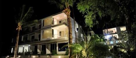 Un edificio de varios pisos con balcones, piscina y palmeras.