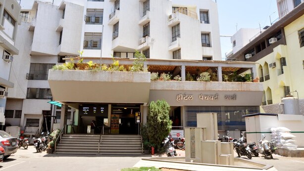 A hotel entrance with a staircase leading up to the door, surrounded by parked motorcycles and a few cars. - Hotel Panchavati Yatri (Nashik)