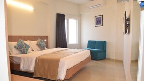 A hotel room with a large bed, a bedside table, a chair, a window with curtains, and a wall-mounted TV. - Hotel Panchavati Yatri (Nashik)