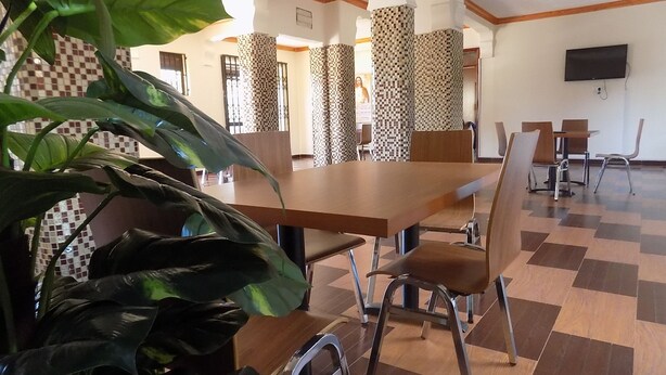 A dining area with a large table and chairs, checkered floor tiles, and a television mounted on the wall. - Olina Hotel and Apartments (Kampala)